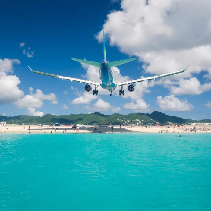 Airplane landing over Maho Beach in Beach in Stint Maarten with turquoise waters in the foreground.